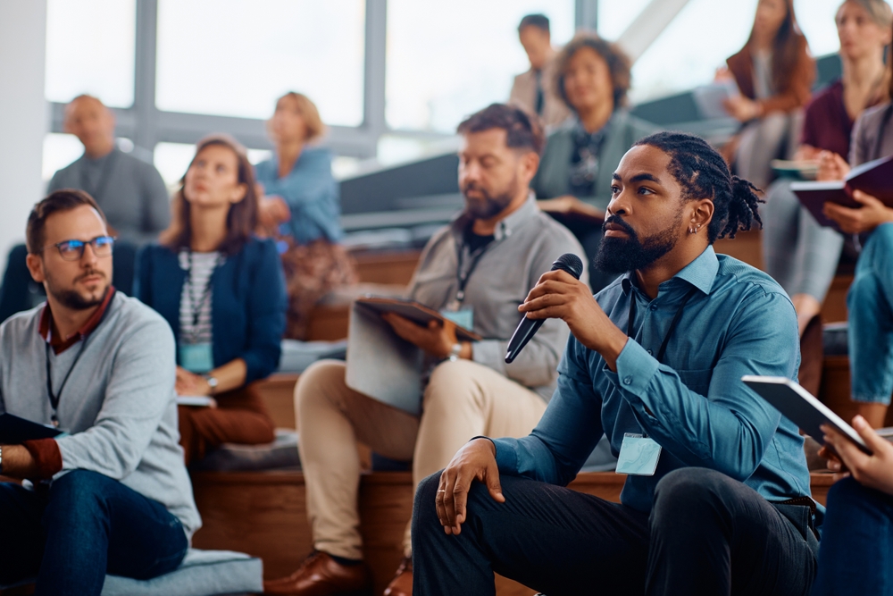 African,American,Business,Seminar,Attendee,Talking,On,Microphone,While,Sitting individuals asking questions at conference